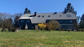 Un grand bâtiment à deux étages, doté d’un toit en tuiles, d’une base en pierre et d’une pelouse verdoyante avec des tables de pique-nique.