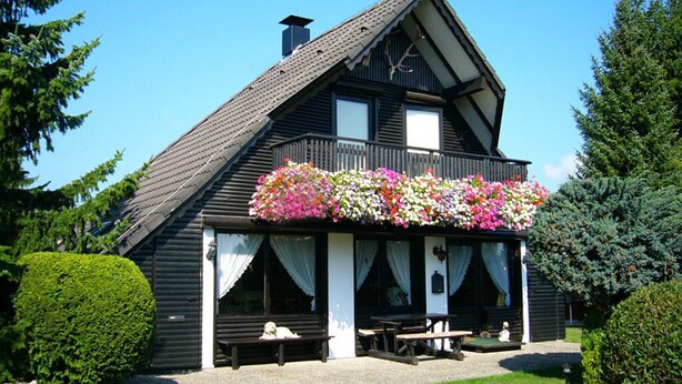 A traditional wooden house with a balcony adorned with colorful flowers, a covered porch, and a small outdoor seating area. - Holiday Home Country House Kathy (Michelstadt)