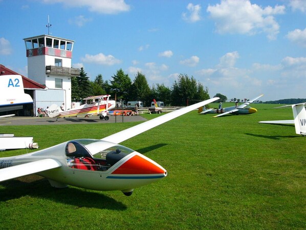 A small aircraft on a grassy field with a control tower in the background.