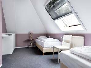 Ein Schlafzimmer mit schrägem Dach, einem Bett, einem kleinen Tisch, einer Lampe und einer Heizung.
