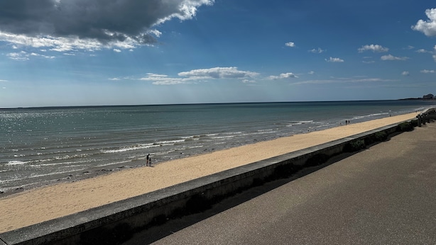 Une plage avec une promenade en béton qui longe le bord de l’eau.
