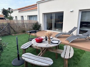 Eine Terrasse mit Holztisch und -stühlen, einem roten Topf und einem Grill.