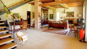 Un'ampia zona giorno con soffitto alto, travi in legno a vista, una scala con ringhiera e un camino.