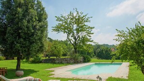 Un giardino sul retro con una piscina, due poltrone relax, un cane e un muro in pietra.