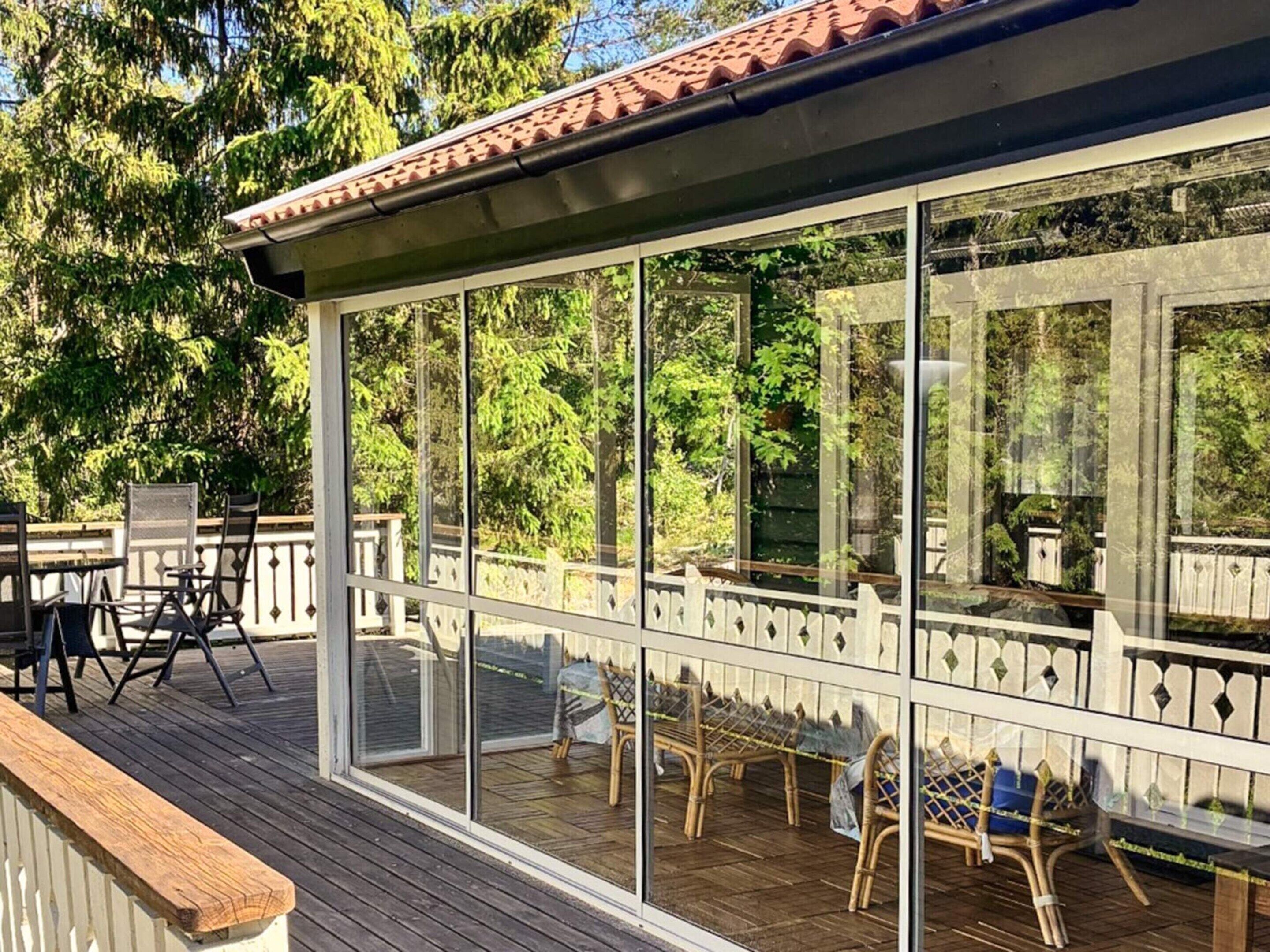 Une terrasse extérieure couverte, dotée de murs en verre, de meubles en bois et d’une rambarde.