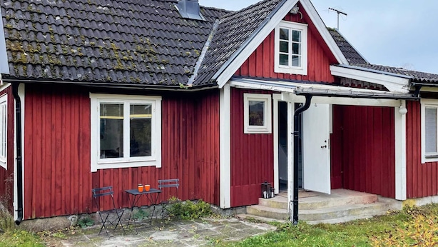 Una casa roja con techo inclinado, una chimenea y un pequeño porche con mesa y sillas.