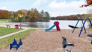 Un parque infantil con columpios y toboganes, un banco y un sendero que lleva a una masa de agua.