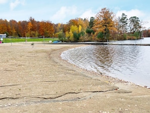 A lakeside area with a sandy shore, a dock, and trees with autumn foliage. - 10 Person Holiday Home in Kyrkhult (Kyrkhult)
