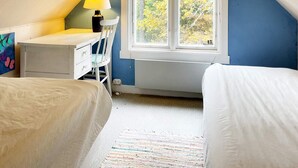 Un dormitorio con escritorio, una silla, un ventanal con vistas a árboles y una cama.
