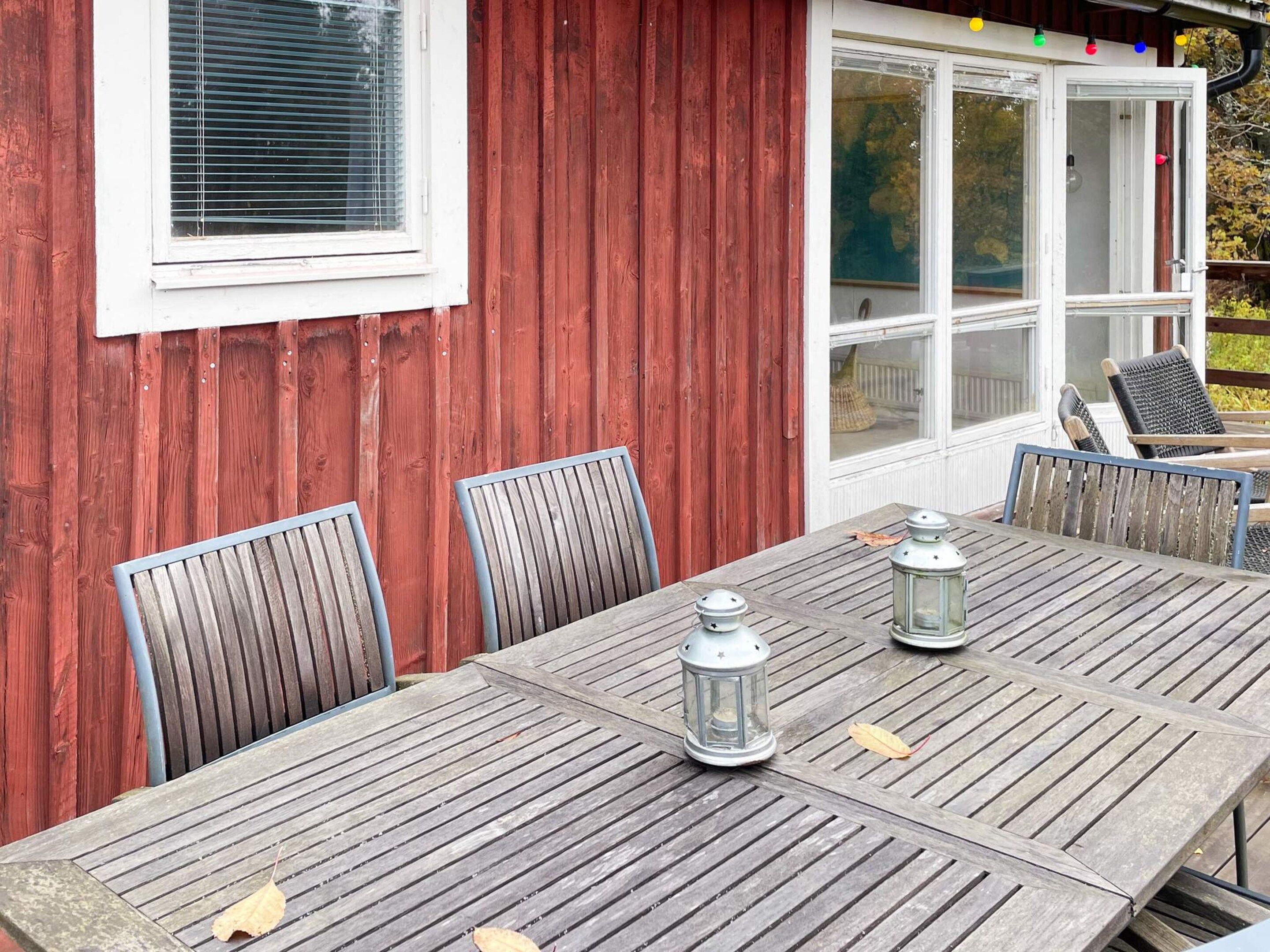 A wooden table with metal chairs and two lanterns, set against a red wooden wall with a window and a door.