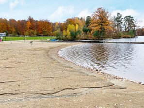 A lakeside area with a sandy shore, a dock, and trees with autumn foliage. - 10 Person Holiday Home in Kyrkhult (Kyrkhult)