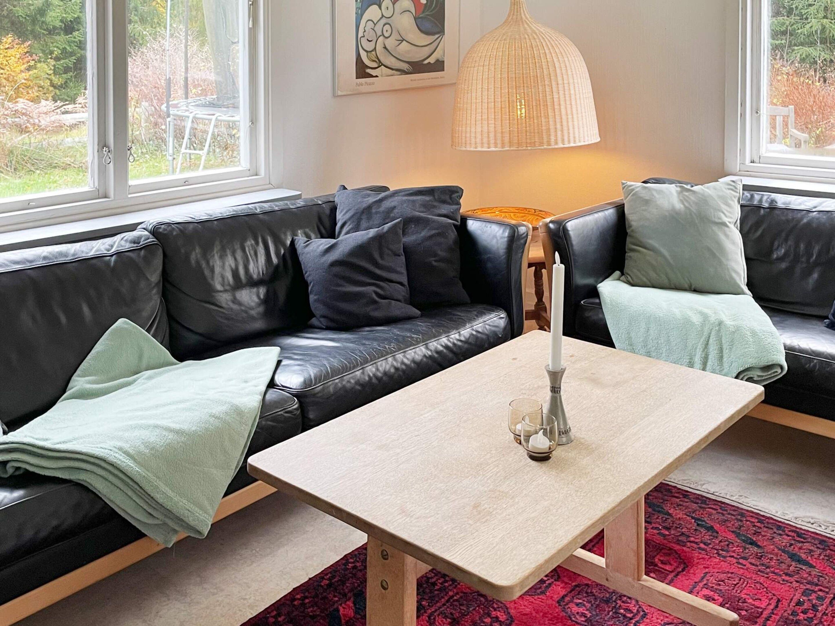 Ein modernes Wohnzimmer mit einem schwarzen Ledersofa, einem hellen Couchtisch und einem roten Teppich mit Muster.