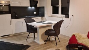 Et moderne køkken med hvide skabe, en sort bordplade og et spiseområde med et hvidt bord og to stole.