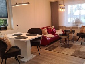 Ein modernes Wohnzimmer mit einem weißen Esstisch, schwarzen Stühlen, einem roten Sofa mit Zierkissen und einem schwarzen Couchtisch.