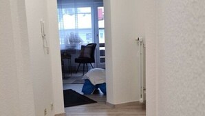 En gang med trægulv, sort måtte og hvid væg.