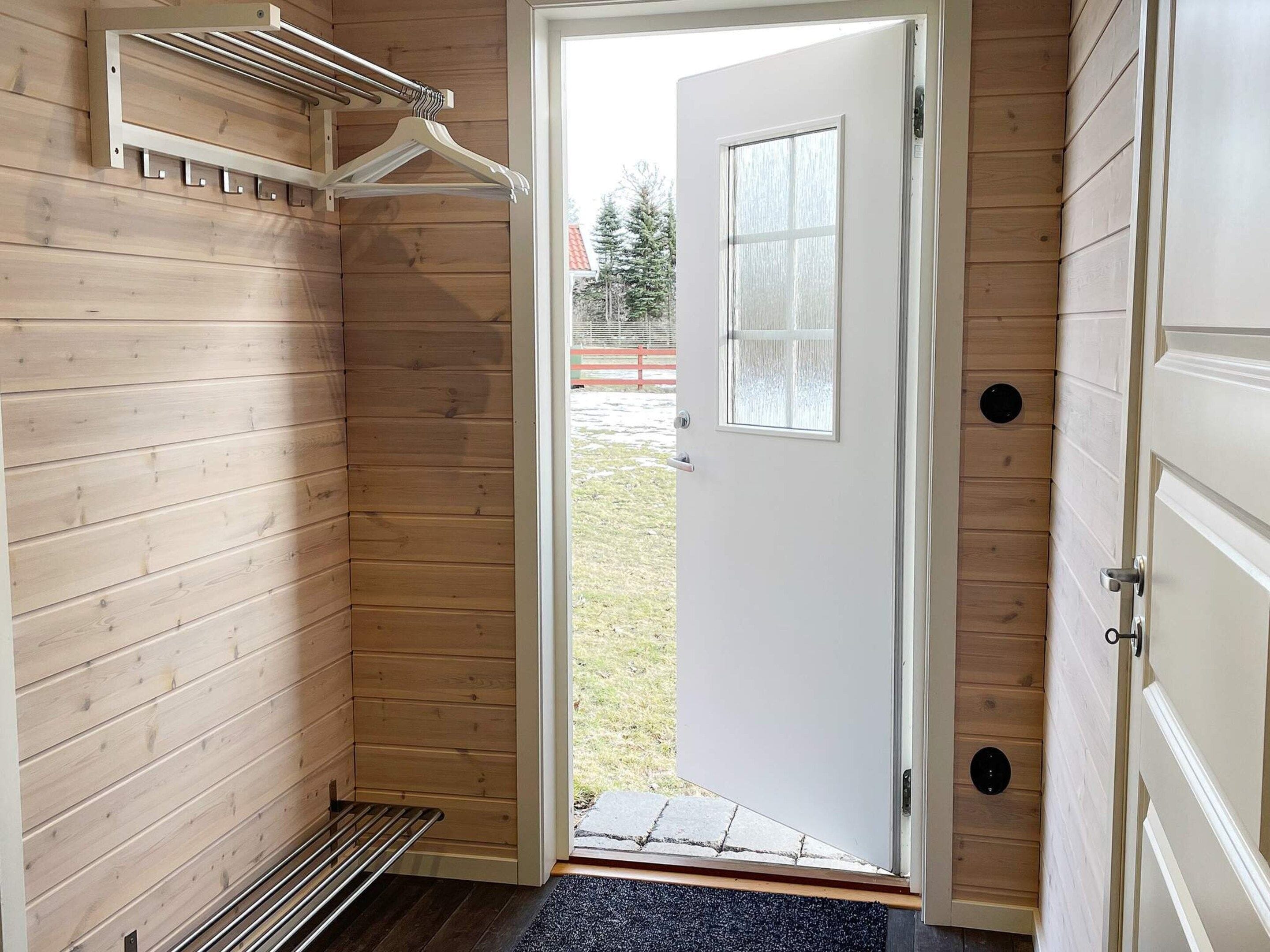 A wooden interior with a door leading outside, a coat rack, and a small window.
