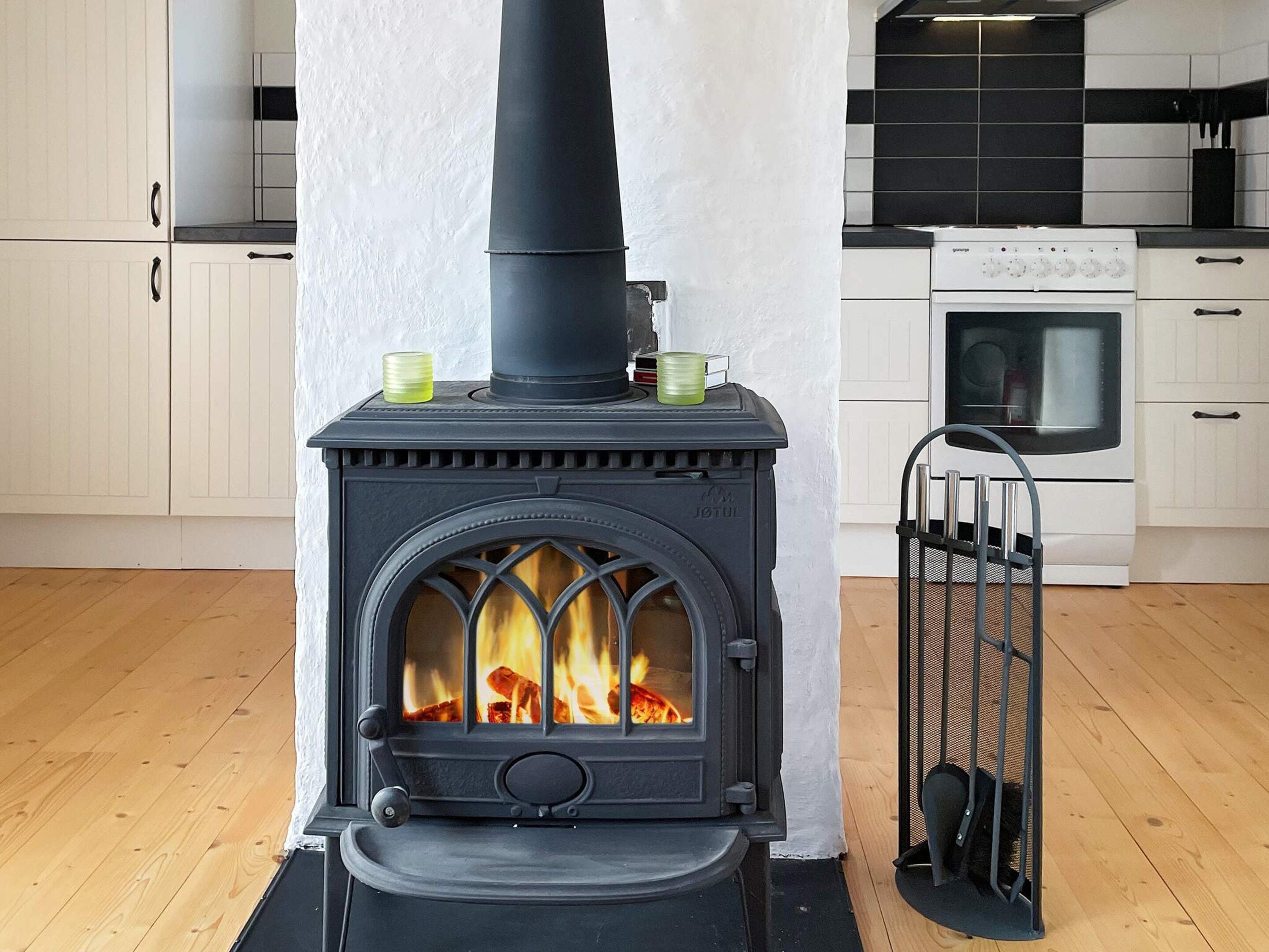 A wood-burning stove with a chimney, a white oven, and a metal gate in a kitchen.