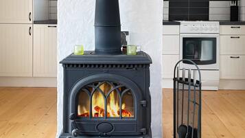 A wood-burning stove with a chimney, a white oven, and a metal gate in a kitchen.