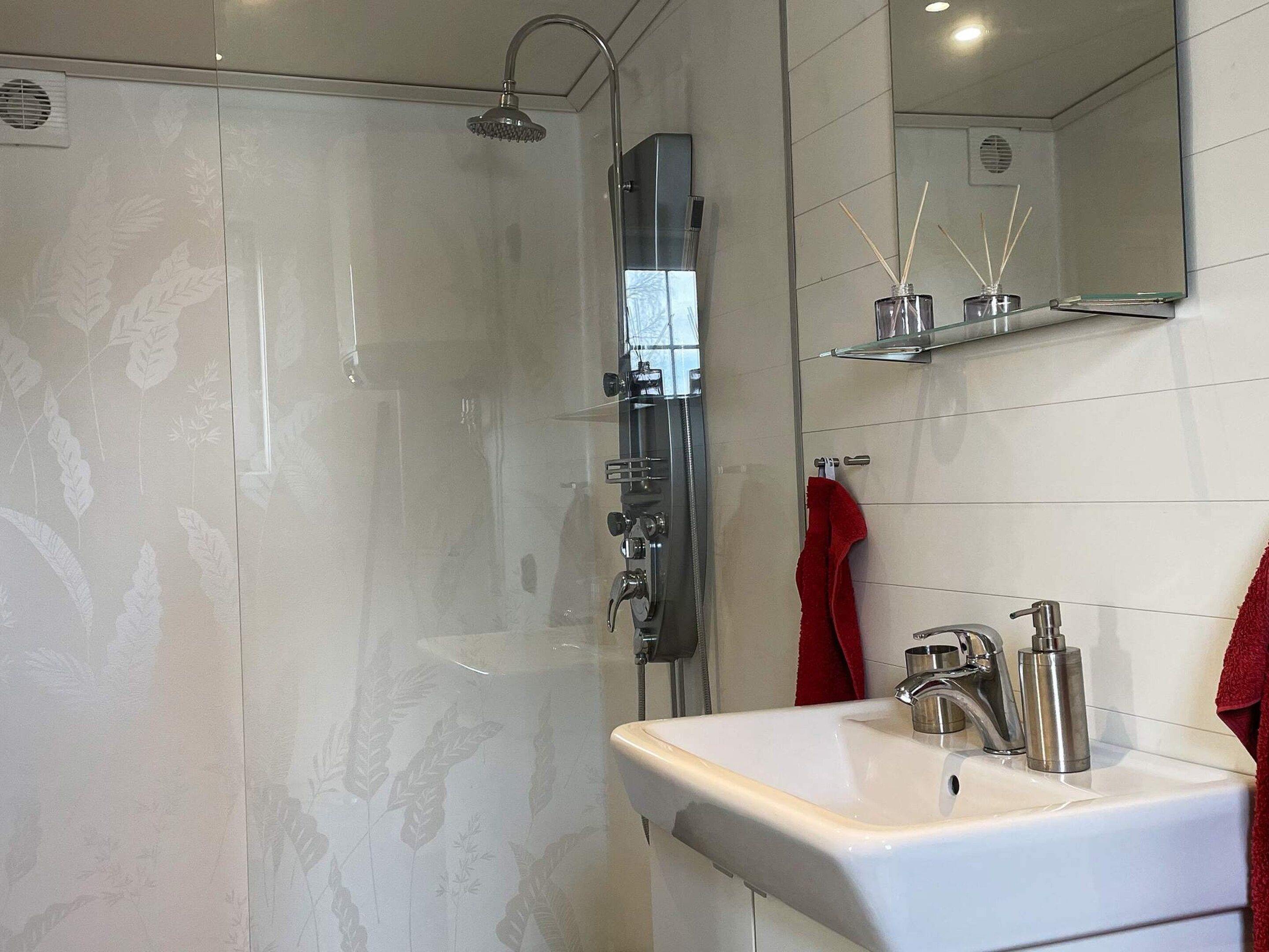Ein modernes Badezimmer mit einer ein Glasfach abgetrennten Dusche, einem weißen Waschbecken mit Chromarmatur und einem Spiegel über dem Waschbecken.