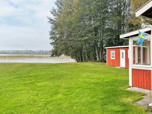 A red building with a white door and windows, a grassy yard, and a flag. - 3 Person Holiday Home in Grimstorp (Grimstorp)
