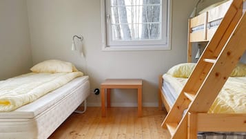 A room with two beds, a wooden bench, a window, and a wall-mounted lamp.