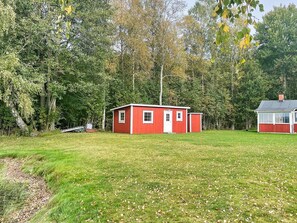 A red wooden cabin with a white door and windows, surrounded by a grassy field and dense trees. - 3 Person Holiday Home in Grimstorp (Grimstorp)