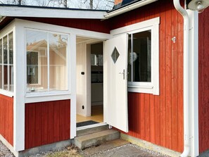 A red wooden building with a white door and windows, a visible kitchen area, and a small porch. - 3 Person Holiday Home in Grimstorp (Grimstorp)