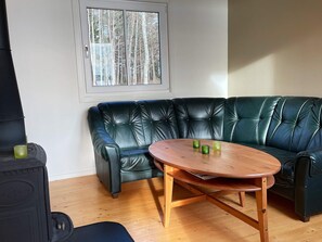 A room with a green leather sofa, a wooden table, and a window with a view of trees. - 3 Person Holiday Home in Grimstorp (Grimstorp)