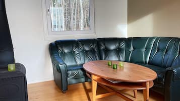 A room with a black leather sofa, a wooden table, and a window with a view of trees.