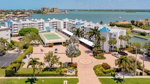 A hotel with multiple buildings, a central courtyard, and a marina with boats in the background. - The Grand-est Bay Condo I Waterfront Bliss (Marco Island)