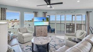 A spacious living room with a large TV, comfortable seating, and a view of the marina. - The Grand-est Bay Condo I Waterfront Bliss (Marco Island)