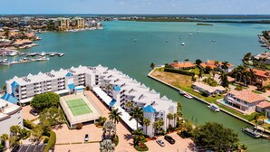A coastal hotel with multiple buildings, a marina with boats, and a tennis court. - The Grand-est Bay Condo I Waterfront Bliss (Marco Island)