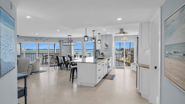 A spacious kitchen with a large island, modern pendant lights, and a view of the ocean through large windows. - The Grand-est Bay Condo I Waterfront Bliss (Marco Island)