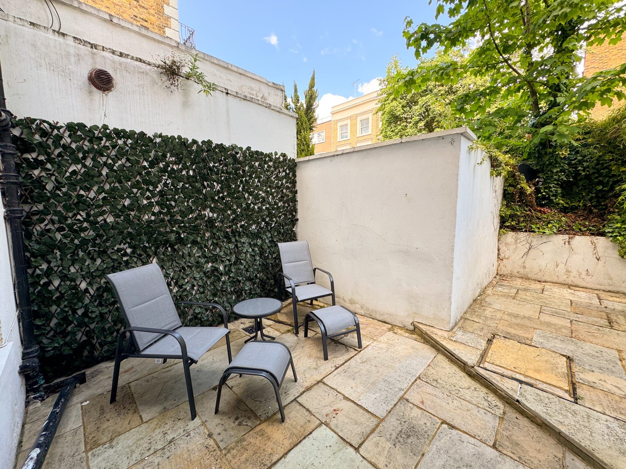 Un espace extérieur aménagé avec un sol en pierre, deux chaises et une petite table.