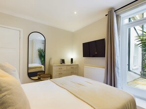 A bedroom with a bed, a dresser, a mirror, a TV, and a window with curtains. - Serene Garden Retreat by Warwick Avenue (Greater London)