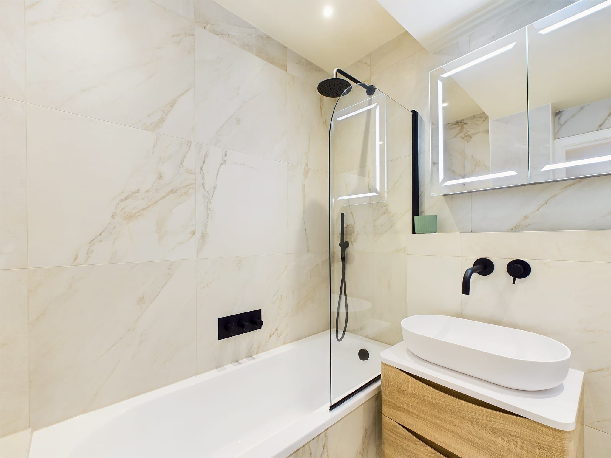 Een moderne badkamer met een witte badkuip, een douche met glazen wanden en een wastafelmeubel met een witte wastafel.