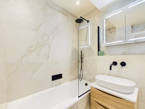 Et moderne badeværelse med et fritstående badekar, en glasafskærmet bruseniche og et toiletbord med vask i hvidt og et træskab.