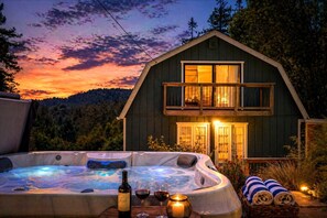 Une cabane en bois à deux étages, dotée d’un bain à remous et d’un balcon, entourée d’arbres et offrant une vue imprenable sur le coucher de soleil.