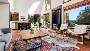 A spacious living area with a large window, a fireplace, and a dining area. - MagicMountain~River Hideaway~View~Hot Tub~Dog~Summer Magic Retreat! EV Charge (Cazadero)
