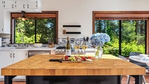 A modern kitchen with a large island, wooden cabinets, and large windows overlooking a forest. - MagicMountain~River Hideaway~View~Hot Tub~Dog~Summer Magic Retreat! EV Charge (Cazadero)