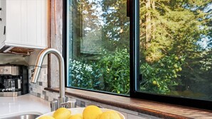 A kitchen with a bowl of lemons, a coffee maker, and a window with a view of greenery. - MagicMountain~River Hideaway~View~Hot Tub~Dog~Summer Magic Retreat! EV Charge (Cazadero)