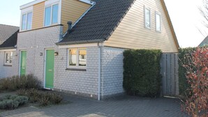 A two-story house with a sloped roof, a green door, and a small window. - Nice Holiday Home 200m. From the Beach (Wemeldinge)