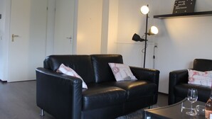 A modern living room with a black leather sofa, a coffee table, and a floor lamp. There is a sign on the wall indicating WiFi availability. - Nice Holiday Home 200m. From the Beach (Wemeldinge)