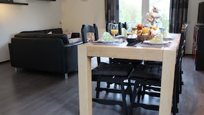A dining area with a table set for four, a black sofa, and a clock on the wall. - Nice Holiday Home 200m. From the Beach (Wemeldinge)