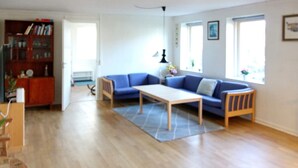 A spacious living room with a wooden floor, a blue sofa, a coffee table, and a bookshelf. - 4 Person Holiday Home in Hadsund (Hadsund)