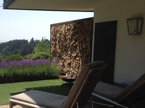 Eine Terrasse mit zwei Loungestühlen, einer Feuerstelle und einer dekorativen Wand aus gestapelten Holzstämmen.