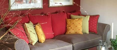 A grey sofa with red and yellow cushions, a glass coffee table, and framed artwork on the wall.