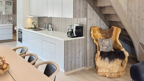 A modern kitchen with white cabinets, a wooden dining table, and a unique, sculptural chair with a fur throw. - 8 Person Holiday Home in Hovden-by Traum (Bykle)