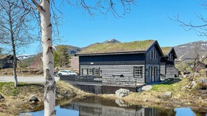 A log cabin with a reflective pond in front, surrounded by mountains and sparse vegetation. - 8 Person Holiday Home in Hovden-by Traum (Bykle)