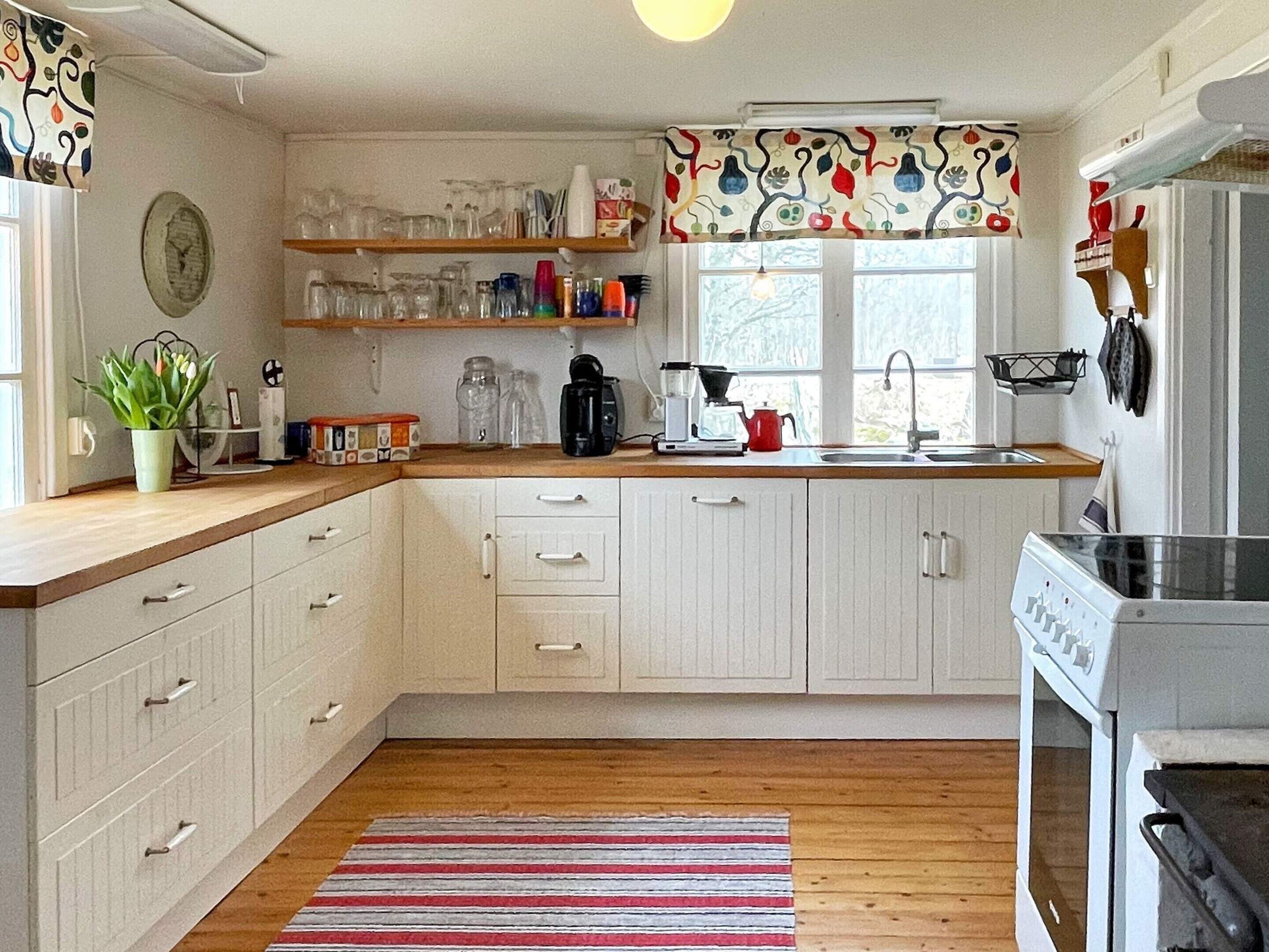 Una cocina con armarios blancos, encimera de madera, un hervidor rojo y un tapete a rayas.